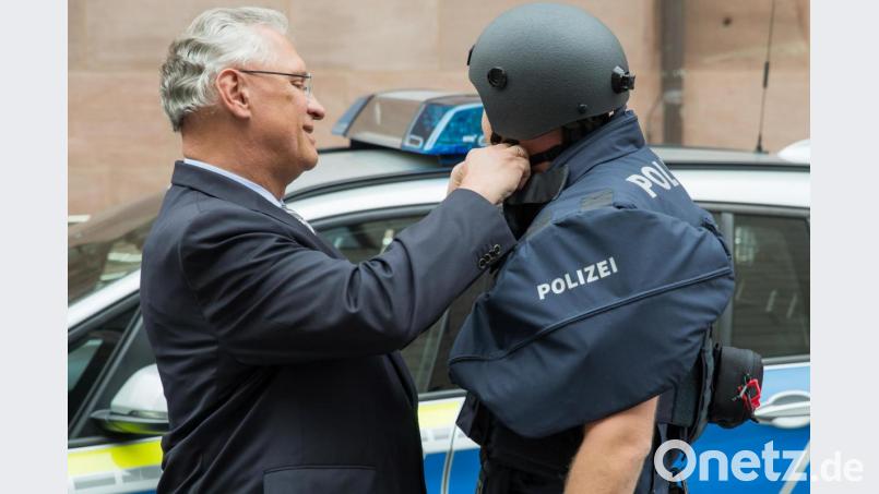 Der bayerische Innenminister Joachim Herrmann (CSU) hilft einem Polizisten mit Kugelsicherer Weste einen neuen ballistischen Schutzhelm zu schließen. Bild: Daniel Karmann/dpa