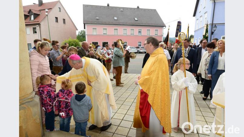 Vor dem Einzug in die Stadtpfarrkirche St. Sigismund segnet Weihbischof Reinhard Pappenberger Kinder, die mit ihren Müttern am Portal des Gotteshauses warten. Stadtpfarrer Pater Hans Ring (rechts) sieht mit großer Freude die Begegnung des Weihbischofs mit den Bürgern Pleysteins. Bild: bey