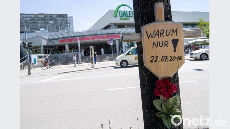 Ein Holzkreuz mit einem Schild und der Aufschrift &quot;Warum nur! - 22.07.2016&quot; hängt vor dem Eingang zum Olympia-Einkaufszentrum (OEZ). Bild:  Peter Kneffel/dpa