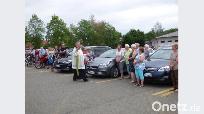 Segen für alles, was Räder hat: Pfarrer Edmund Prechtl segnet alle Autos, Fahrräder und Motorroller, die sich auf dem Rewe-Parkplatz aufreihen. Bild: mng