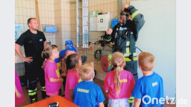 Zwei Feuerwehrmänner zeigen den Kindern Ausrüstungsgegenstände im Feuerwehrhaus. Bild: tu