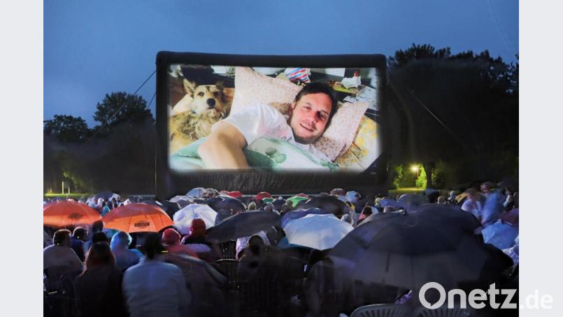 Die Open-Air-Kinobesucher sind mit Regenschirmen, Capes und wasserdichten Jacken für den heftigen Regenguss gerüstet und lassen sich ihren „Leberkäsjunkie“ nicht vermiesen. Bild: Gerhard Götz