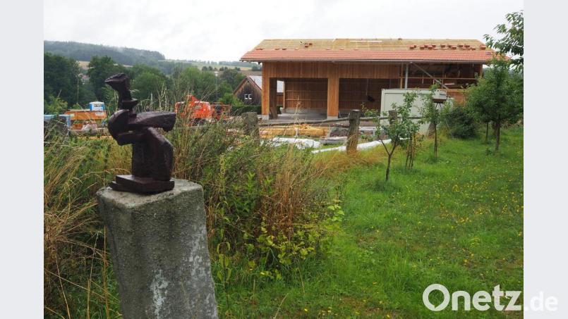 Eine Maschinenhalle mit Holzlager verstellt vom Garten des Zehentstadel aus gesehen den Blick auf grüne Hügel. Bild: bl