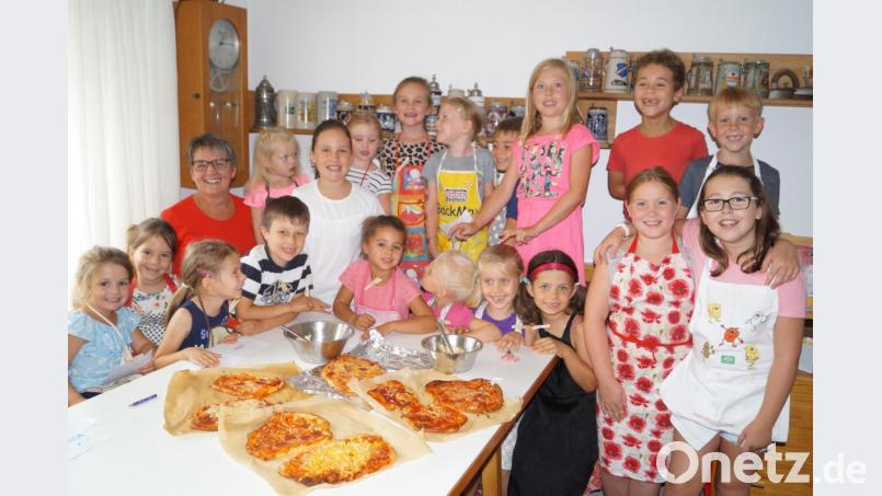 Stolz präsentieren die 15 Kinder mit Kursleiterin Doris Bock (hinten, links) ihre Pizza-Kreationen, die anschließend in den Backofen wandern. Bild: du