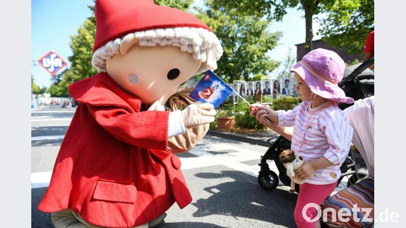 Eine Sandmännchen begrüßt ein Mädchen, das eine Sandmännchenfahne in der Hand hält, bei dem Geburtstagsfest zum 60. Geburtstag des Sandmanns im Filmpark Babelsberg. Bild: Julian Stähle/dpa