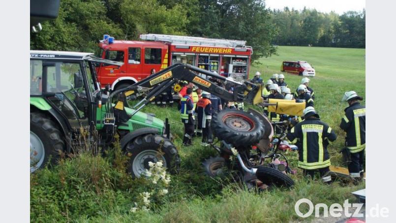 In einem kleinen Bachlauf neben der Straße stürzte der Traktor älteren Baujahres um. Rettungskräfte mehrerer Feuerwehren kümmerten sich dann um die Bergung der beiden Verletzten. Behilflich war dabei auch ein Landwirt mit seinem Bulldog (links). Bild: exb/Feuerwehr im Landkreis Schwandorf