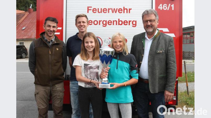Franziska Götz (vorne, links) und Magdalena Woppmann strahlen, als ihnen Bürgermeister Johann Maurer (rechts) den Siegerpokal übergibt. Dabei lobt der Rathauschef die vorzügliche Organisation der Feuerwehr Georgenberg um die Kommandanten Dominik Schmid und Oswald Hamann (weiter von rechts). Bild: pi