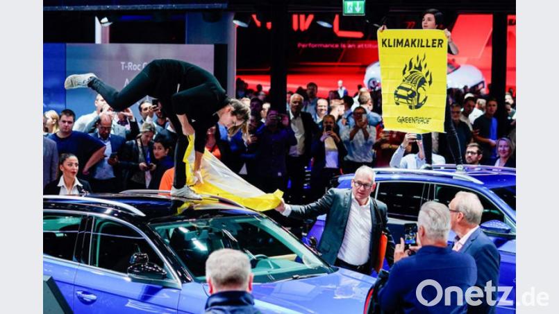 Während des Eröffnungsrundgangs von Bundeskanzlerin Merkel (CDU) auf der IAA versucht ein Mann am Stand von Volkswagen einer Aktivistin der Umweltschutzorganisation Greenpeace ihr Transparent mit der Aufschrift „Klimakiller“ zu entreißen. Bild: Uwe Anspach/dpa