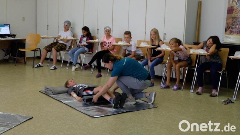 Natalie Wölfl vom Jugendrotkreuz zeigt den Fünftklässlern der Otto-Wels-Mittelschule Mitterteich, wie bei Bauchschmerzen mit der „Knierolle“ der Patienten in eine Schonhaltung gebracht werden kann. Bild: exb/Bayerisches Rotes Kreuz Kreisverband Tirschenreuth
