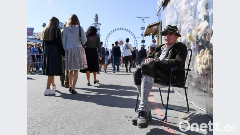 Ein Standbesitzer sitzt in Tracht neben seinem Souvenirstand auf einem Stuhl. Bild: Tobias Hase/dpa
