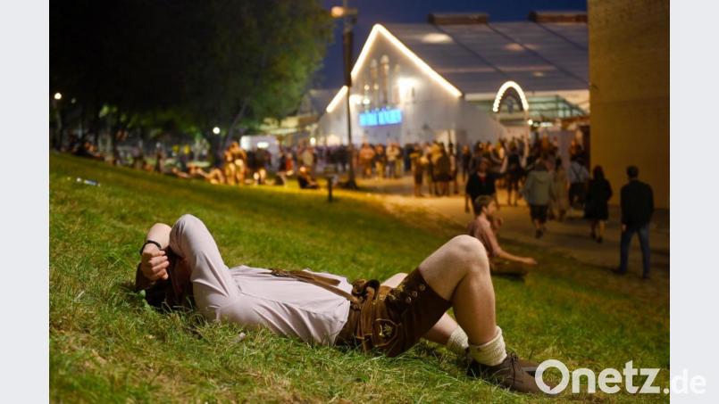 Platt: Ein Besucher in Lederhose liegt am Rande des Oktoberfests am Abend auf einer Wiese. Bild: Tobias Hase/dpa