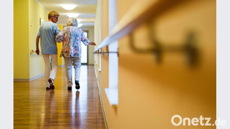 Eine Pflegekraft geht in einem Pflegeheim mit einer älteren Dame über einen Korridor. Bild: Christoph Schmidt/dpa