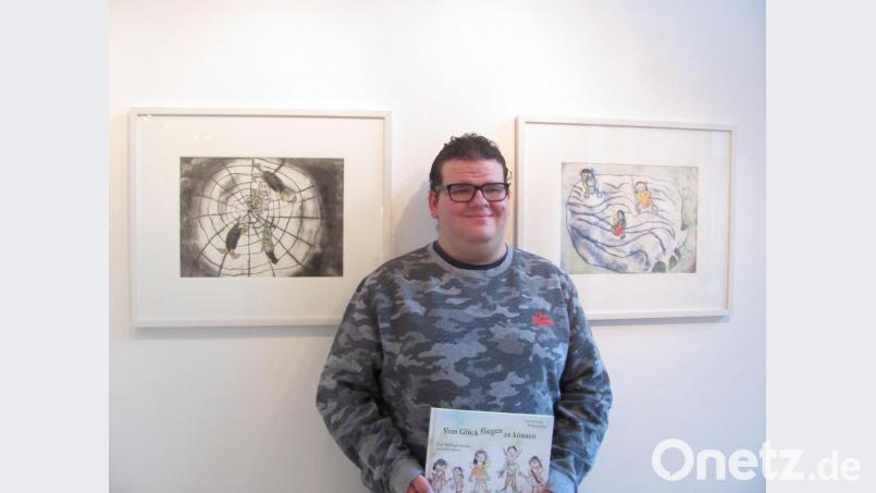 Wolfgang Bauer zeigt das Buch „Vom Glück, fliegen zu können“ im Kunstbau Weiden zwischen den Originalillustrationen „Spinnennetz“ und „Befreite Elfen“ in der Ausstellung „Kunst in der Kapelle“. Bild: rbr