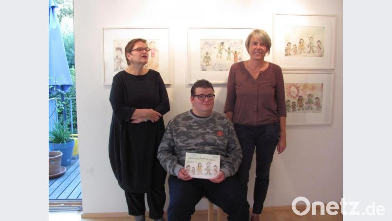 Die den Künstler betreuende Heilpädagogin Renate Höning, Wolfgang Bauer mit dem illustrierten Buch und die Kunstpädagogin Irene Fritz (von links) eröffnen die Ausstellung „Vom Glück, fliegen zu können“. Bild: rbr