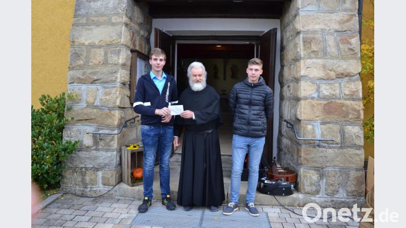 Die Oberministranten Tobias Hofmeister (links) und Johannes Eger (rechts) überreichen die Spende an Pater Ferdinand. Bild: gi