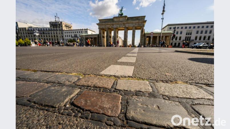 An der Stelle, wo zu DDR-Zeiten die Berliner Mauer stand, sind vor dem Brandenburger Tor Pflastersteine, die an die Mauerzeiten erinnern. Eine Schwelle mit Pflastersteinen zeichnet die Grenze zwischen Ost und West nach. Bild: Christophe Gateau/dpa