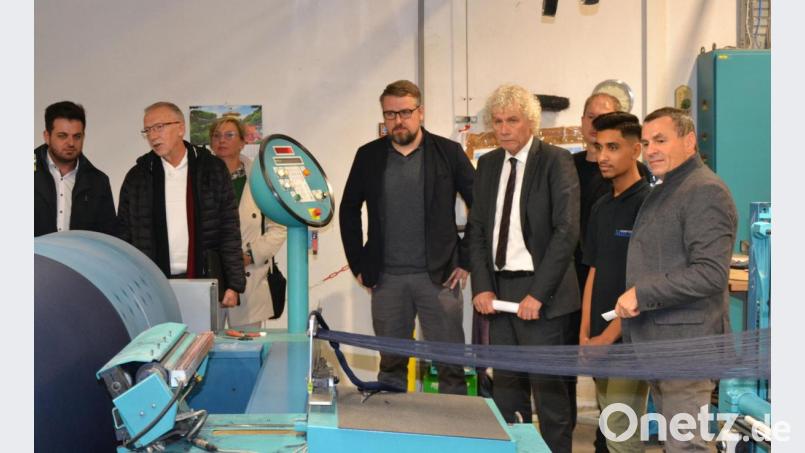 Die Fäden laufen durch die Maschine. Die Besucher samt Landrat Wolfgang Lippert und Azubi Mohammed schauen gespannt zu. Bild: Susanne Forster