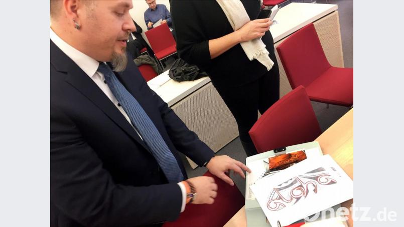 Polizeioberkommissar Jürgen Prichta hält bei der Verhandlung am Bayerischen Verwaltungsgerichthof die Entwürfe für sein geplantes Tattoo in den Händen. Der Beamte zieht vor Gericht, weil er sich den Schriftzug «Aloha» auf den Unterarm tätowieren lassen will, was laut Bayerischem Beamtengesetz verboten ist. Die Gewerkschaft der Polizei erwartet ein Grundsatz-Urteil. Bild: Britta Schultejans/dpa