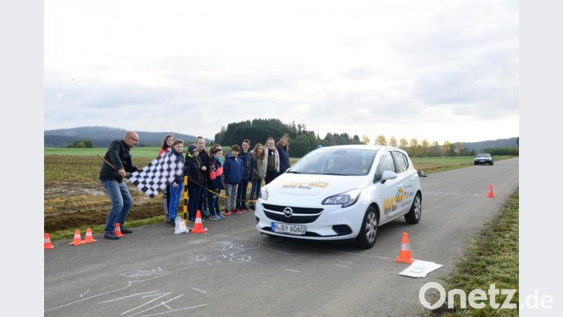 André Helwig, ADAC Nordbayern, sitzt am Steuer, Matthias Kastner, ADA Weiden, schwenkt die Zielflagge: Nach der Vollbremsung zeigt sich, wie lange der Bremsweg beim 50 km/h ist. Die Schülerinnen und Schüler beobachten das Bremsmanöver fasziniert. Bild: bey