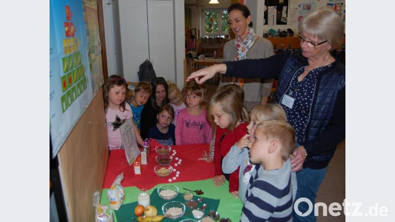 Ökotrophologin Angelika Meindl erklärt den aufmerksamen Kleinen gesunde und weniger gesunde Lebensmittel, die anschaulich auf grünen und roten Deckchen verteilt sind. Mit im Bild Projektmanagerin Anna Lilliu (stehend Mitte). Bild: grm