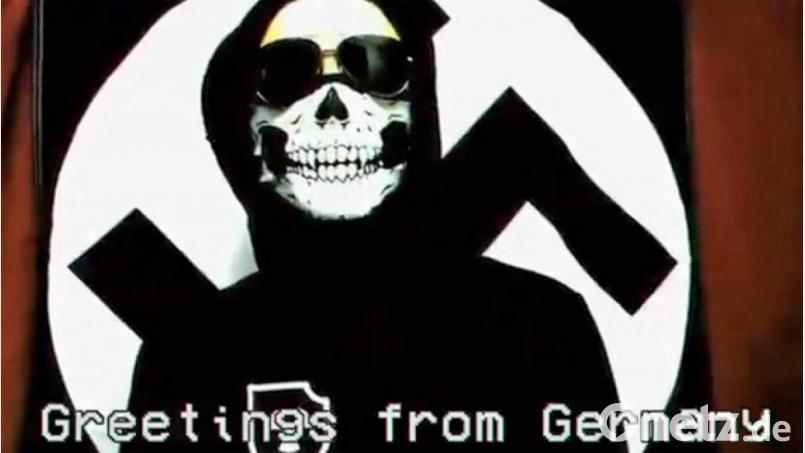 In einem Video, das seit 2018 im Netz kursiert, bezieht sich ein Sprecher auf die „Atomwaffen Division“. Unterlegt von martialischer Musik marschieren vermummte Neonazis. Ein schwarzgekleideter Sprecher mit Totenkopfmaske verkündet vor einer Hakenkreuzflagge: »Der Natio­nalsozialismus lebt trotz einer ganzen Welt, die ihn zerstören will.« Bild: Screenshot Twitter.com