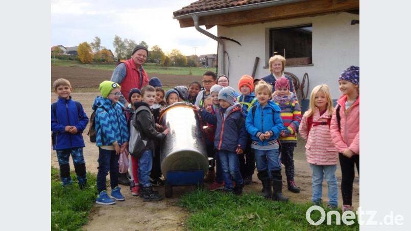 Die Schüler der Klasse 1/2 von der Josef-Voit-Grundschule schieben unter der Anleitung von Landwirt Konrad Reil (Mitte) und der Aufsicht durch Lehrerin Brigitte Böhm (rechts daneben) den großen Milchtank zur Milchtankstelle. Bild: nbu
