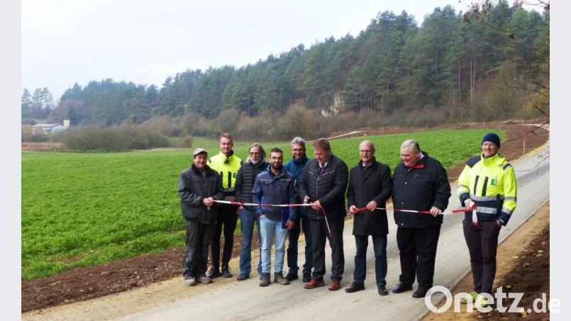 Die beiden Bürgermeister Stefan Braun und Ludwig Lang (Mitte) durchschneiden symbolisch das Absperrband und nehmen die sanierte Gemeindeverbindungsstraße zwischen dem Hallerbrunnen (Hintergrund) und Pattershofen (Kastl) in Betrieb. Sie ist Teil des vielbefahrenen Fünf-Flüsse Radwegs. Bild: jp