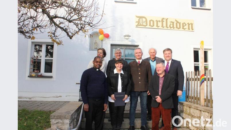 Gäste vor dem Utzenhofener Schmuckstück: dem 1994 eröffneten Dorfladen –damals dem ersten in ganz Bayern
Vorne von links: Pfarrer Peter Lungu, Vorsitzende Christa Forster, Harald Schwarz, Josef Urban. Hinten von links: Gebriele Grunelius-Isak, Werner Penth, Altbürgermeister Hans Raab und Bürgermeister Stefan Braun Bild: aun