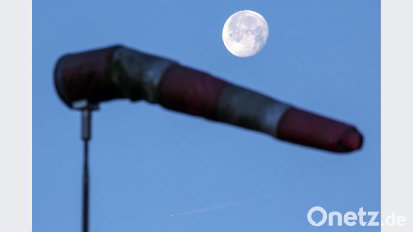 Über einem vom Wind aufgeblasenen Windsack steht kurz nach Sonnenaufgang der Mond. Foto: Thomas Warnack/dpa Bild: Thomas Warnack