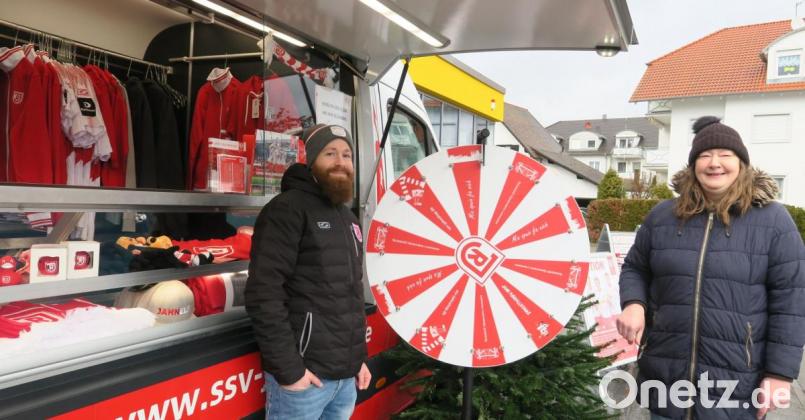 Fanshop-Begleiter Simon Raab (links) ließ Jahn-Fan Tanja Dineiger (rechts) am Glücksrad drehen. Sie gewann eine rote Christbaumkugel mit Jahn-Emblem und kaufte noch weitere dazu. Das Jahn-Mobil machte am Samstag auf dem Netto-Parkplatz Halt. Bild: Hirsch