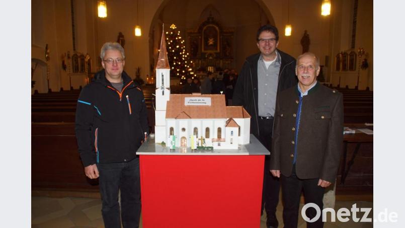 Pfarrer Wolfgang Dietz freute sich über das Engagement von Willibald Kulzer (links) und Hans Mösbauer (rechts), die eine Miniaturausgabe der Pfarrkirche im hinteren Teil des Kirchenschiffes aufstellten. Am Modell haben die Erbauer Fahnen mit den Farben der Stadt und der Kirche vor dem Eingangsportal gehisst. Bild: mmj