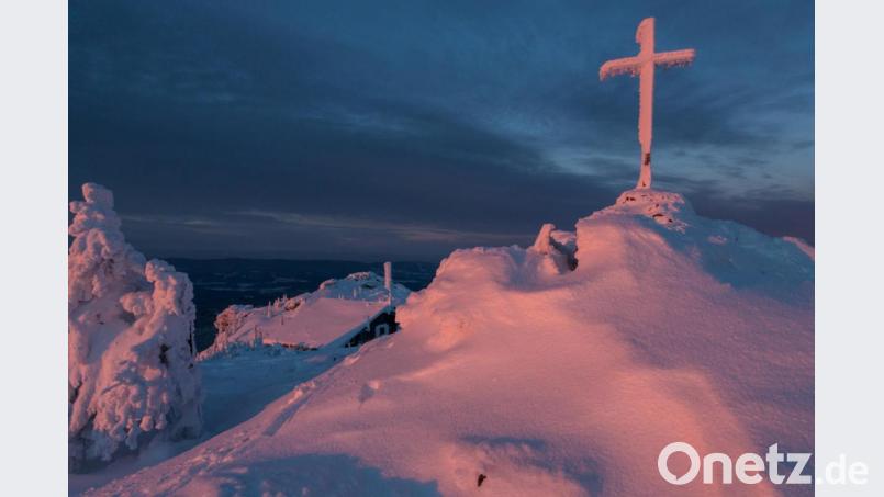 Das Gipfelkreuz am 1660 Meter hohen Arber im Licht der Morgenröte. Himmel und Erde bilden ein magisches Stück Bayerischer Wald. Die Wintersonne malt ein Gemälde, ein Werk mit Schatten und Schnee. Bild: exb/Josef Schell