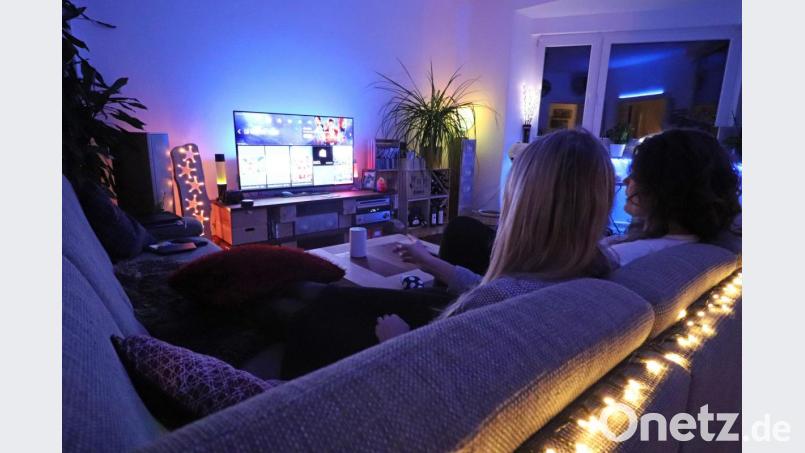 Alexa, mach das Licht blau!“ Zwei Frauen im Wohnzimmer mit Smart TV und LED-Beleuchtung, deren Helligkeit und Farbton sich per Sprachsteuerung anpassen lassen.
(Gestellte Szene) Bild: Nina Drewes/dpa