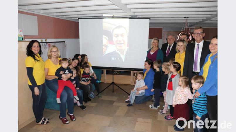 Gratulierten per Videobotschaft Silvia Markowski zum 60. Geburtstag: Ministerpräsident Markus Söder und Bürgermeister Franz Stahl. Vor der Leinwand: Stellvertretende Kinderhausleiterin Maria Üblacker (links), Silvia Markowski (Sechste von rechts), Peter Gold (Fünfter von rechts), Norbert Schuller (Zweiter von rechts) sowie Erzieherinnen und Kinder des Kinderhauses. Bild: exb/Stadt Tirschenreuth/M. Streich