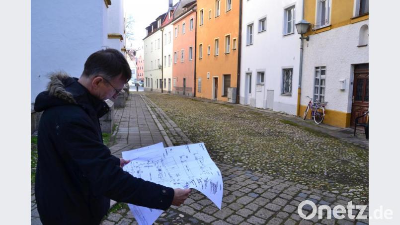 Pfarrer Hans-Martin Meuß studiert den Plan. Der sieht vor, dass der Gehweg auf der Südseite von St. Michael (links zu sehen) verschwindet. Der Gehweg rechts entlang der Häuserzeile „Am Stock“ bleibt. Für die Anwohner werden – von der Schulgasse kommend – zwei Stellplätze zum Be- und Entladen eingerichtet. Bild: Hladik