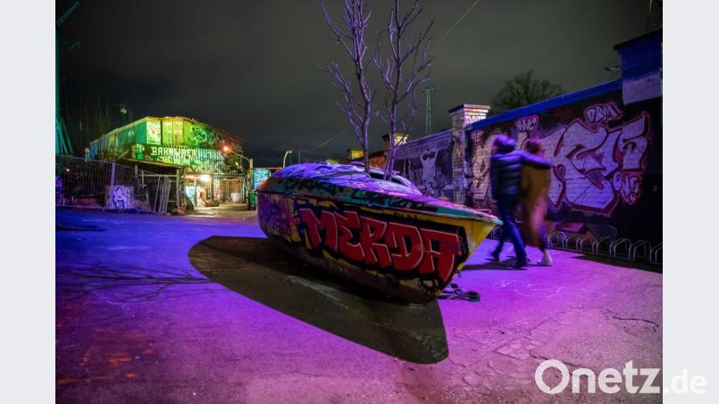 Personen gehen an einem ausrangierten Boot vor dem Eingang des Nachtclubs "Bahnwärter Thiel" vorbei. Bild: Lino Mirgeler/dpa