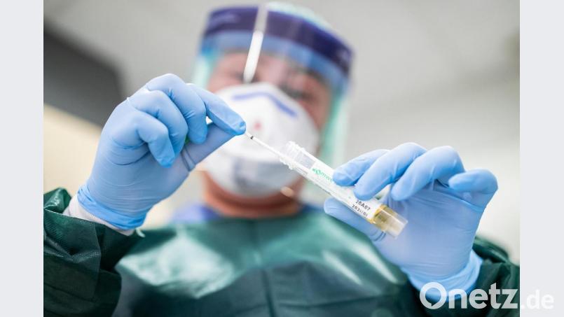 Die Stationsleiterin auf der Infektionsstation eines Krankenhauses steht in Schutzkleidung und mit einer Atemmaske in einer Schleuse und hält ein Abstrichröhrchen in den Händen. Bild: Marcel Kusch/dpa