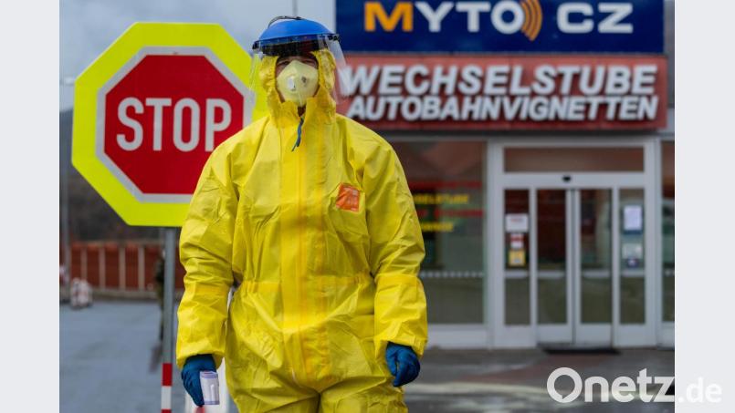 Ein Feuerwehrmann steht in Schutzbekleidung während einer Kontrolle von Reisenden an einer Tankstelle. Bild: Robert Michael/dpa