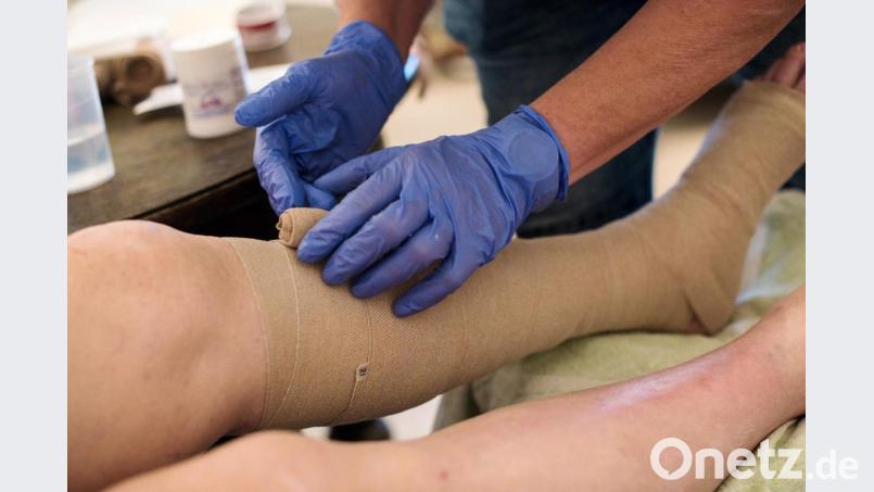 Eine ambulante Pflegerin bandagiert die Beine eines alten Mannes (Symbolbild). Der Landkreis Amberg-Sulzbach und die Stadt Amberg suchen wegen der Corona-Epidemie freiwillige Helfer für den Einsatz im Gesundheitswesen. Bild: Jana Bauch/dpa