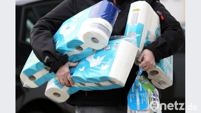 Ein Mann trägt eingekauftes Toilettenpapier und Küchenrollen aus einem Supermarkt. Bild: Rene Traut/dpa