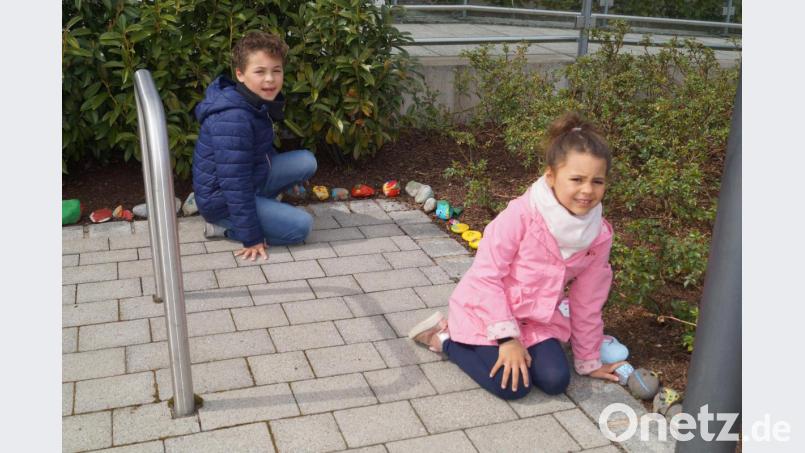Die vierjährige Mia (vorne) und der siebenjährige Elias (hinten) tragen ebenfalls mit bunten Steinen zum Wachsen der &quot;Schlange&quot; rund um das Rathaus bei. Bild: du