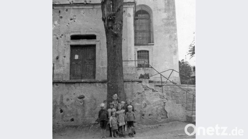 Kinder posieren vor der Pfarrkirche, wo Einschusslöcher deutlich zu sehen sind. Repro: jr
