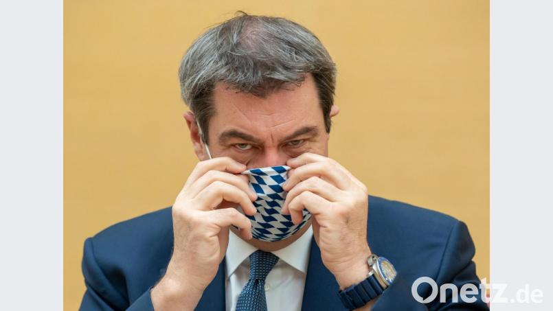 Markus Söder (CSU), Ministerpräsident von Bayern, zieht sich für die Fotografen vor Beginn der Sitzung des bayerischen Landtags eine Mundschutzmaske auf. Bild: Peter Kneffel/dpa