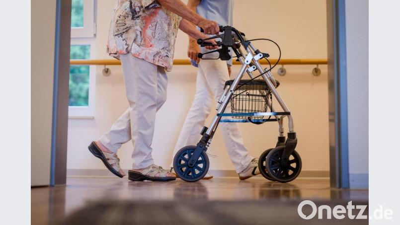 Eine Pflegekraft geht mit einer älteren Frau über einen Korridor in einem Pflegeheim. Viele Pflegekräfte erhalten nun einen Mindestlohn. Bild: Christoph Schmidt