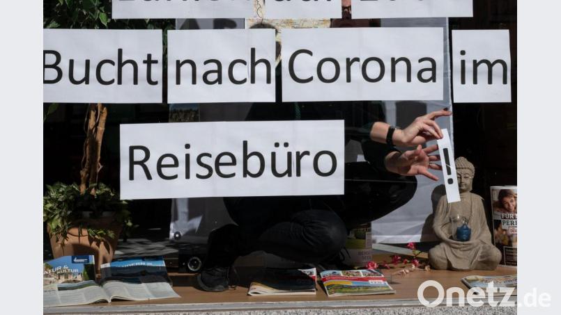 Ein Mitarbeiterin klebt Blätter mit der Aufschrift „Bucht nach Corona im Reisebüro“ in das Schaufenster. Bild: Bernd Thissen/dpa