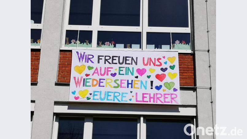 Ein farbenfrohes Tuch, gefertigt von Sabine Lehner, mit der Aufschrift „Wir freuen uns auf ein Wiedersehen! Eure Lehrer“ hängt an der Außenwand der Grundschule und begrüßt die Schüler. Bild: weu