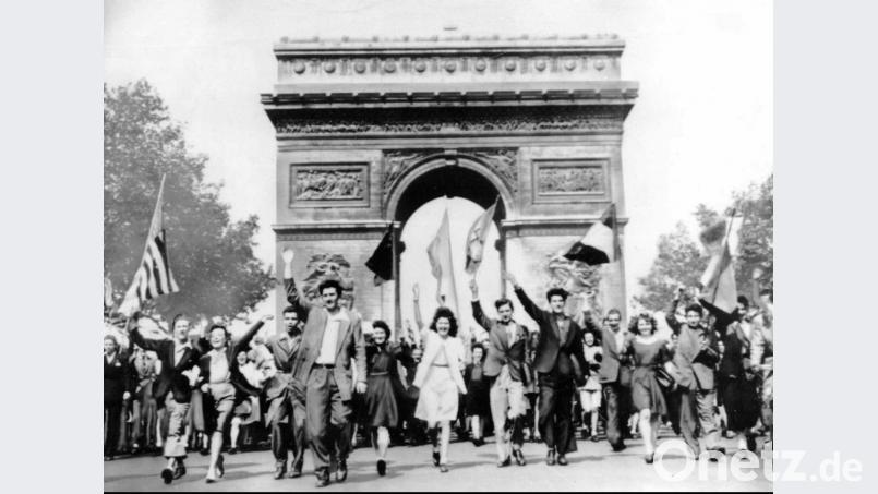 Franzosen schwenken die Nationalflaggen der Alliierten, während sie vor dem &quot;Arc de Triomphe&quot; auf der Straße gehen und die bedingungslose Kapitulation der deutschen Wehrmacht am 08. Mai 1945 feiern. Bild: Uncredited