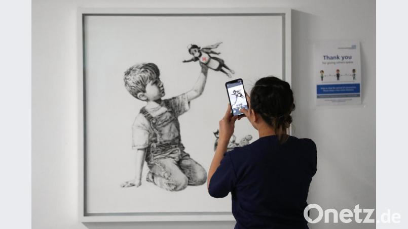 Eine medizinische Mitarbeiterin fotografiert das Banksy-Kunstwerk mit dem Titel „Game Changer“. Foto: Andrew Matthews/PA Wire/dpa Bild: Andrew Matthews