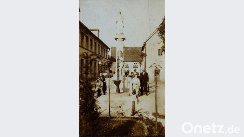 Ein Foto aus den 1920-er Jahren: Die Familie Schertl posiert neben der Mariensäule und dem davor befindlichen Brunnen. Links zu sehen das einstige Knabenschulhaus, rechts die damalige Sakristei der Pfarrkirche Bild: u
