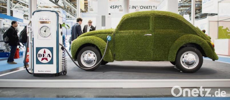 Wie grün ist das E-Auto? Ein Ladekabel steckt in einem mit grünem Kunstrasen überzogenen VW Käfer. Bild: Julian Stratenschulte/dpa
